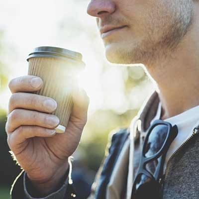 man drinking coffee outdoors in the sunshine