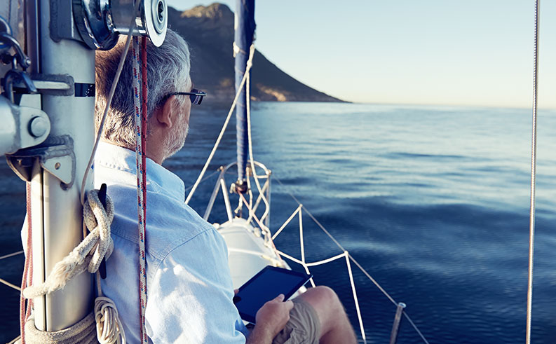 mature man reading a tablet on the bow of a boat