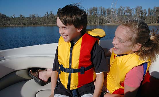 Two smiling kids wearing life jackets enjoy a boat ride