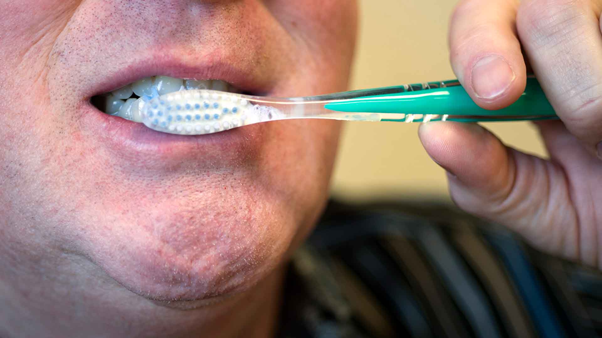 close up of a man brushing his teeth with a toothbrush and toothpaste