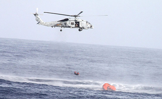 US Navy helicopter hovers above a life raft while performing a search and rescue operation